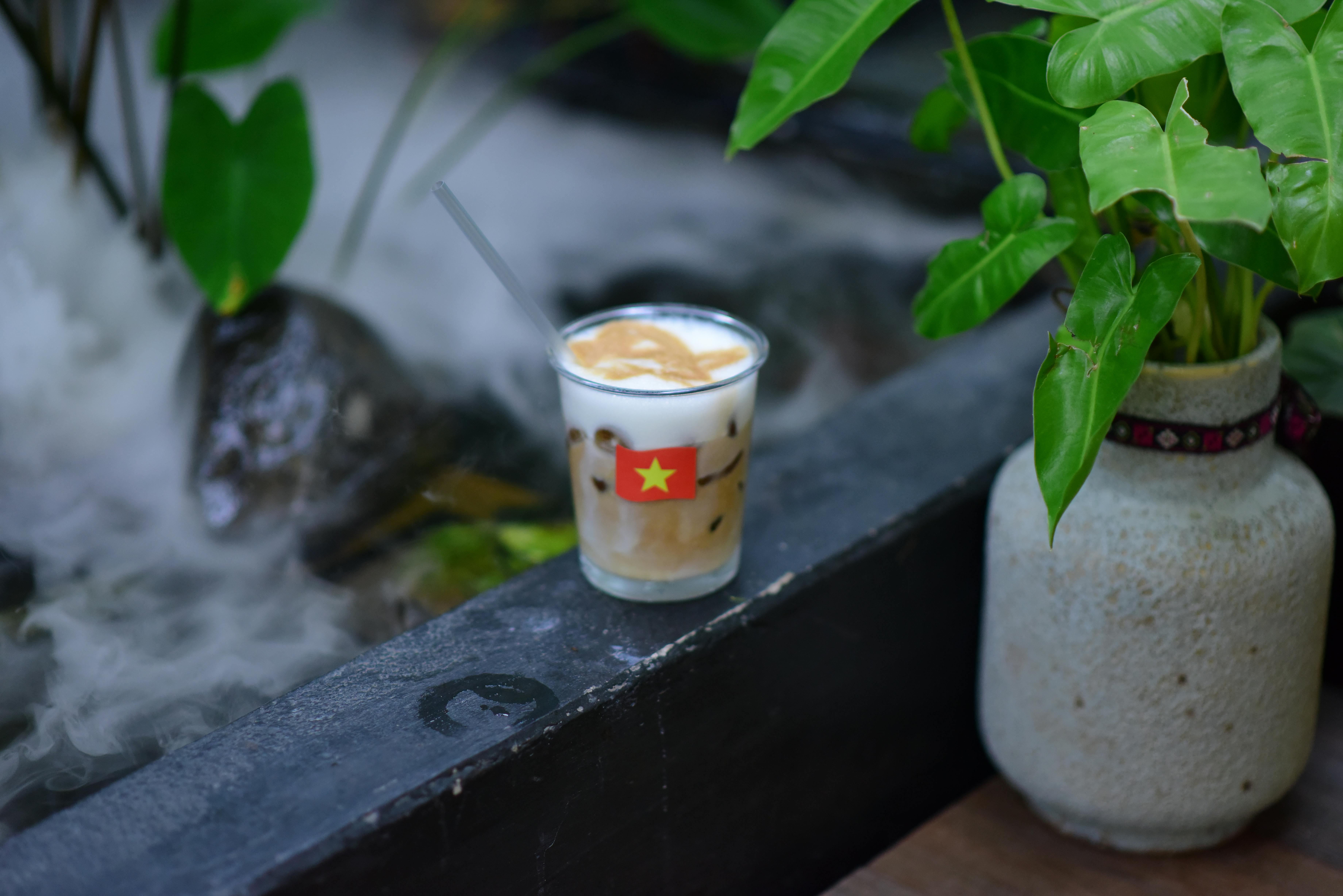 A refreshing Vietnamese iced coffee with a flag design, placed in a serene garden setting.