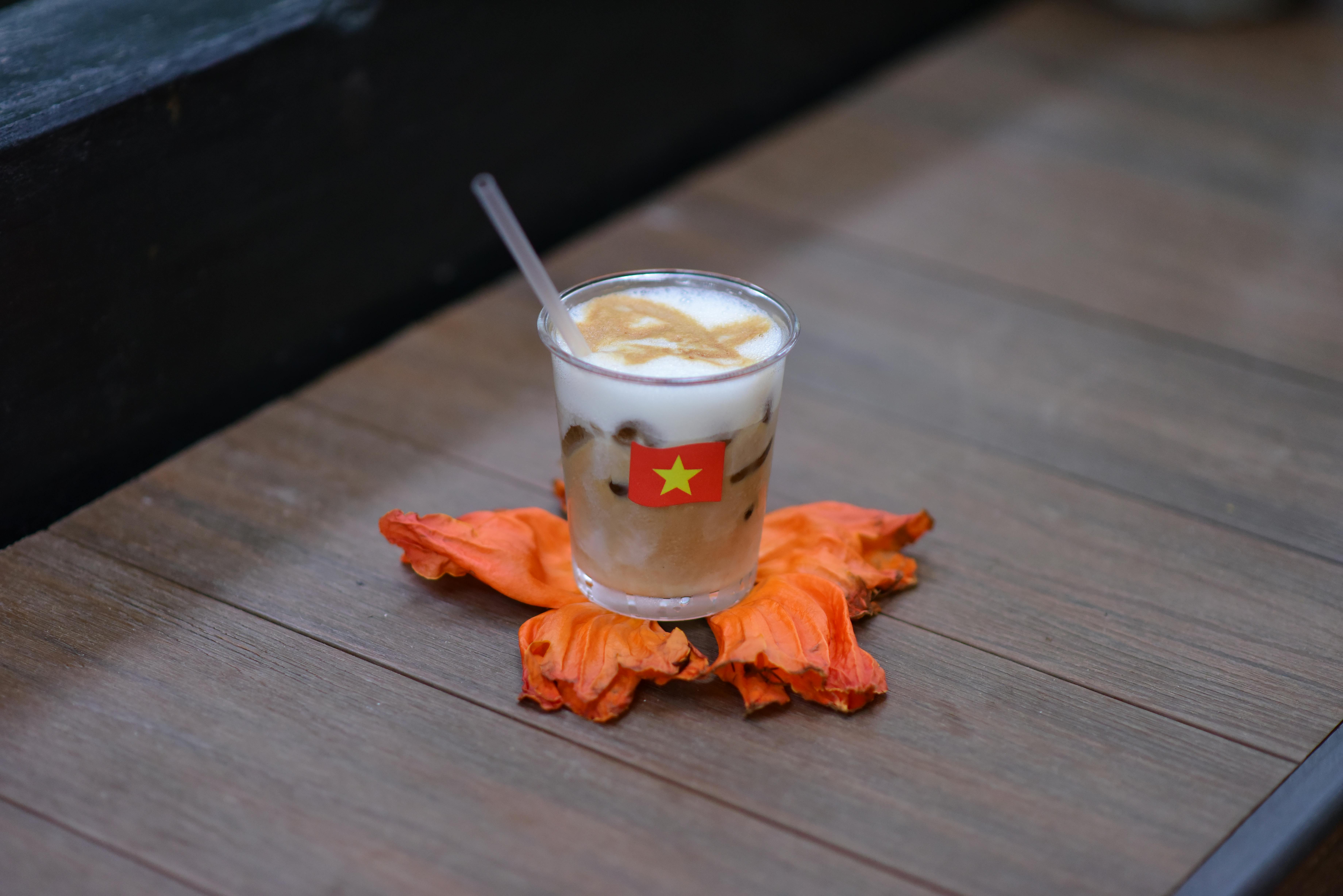 Vietnamese iced coffee served on a vibrant orange petal on wooden table.