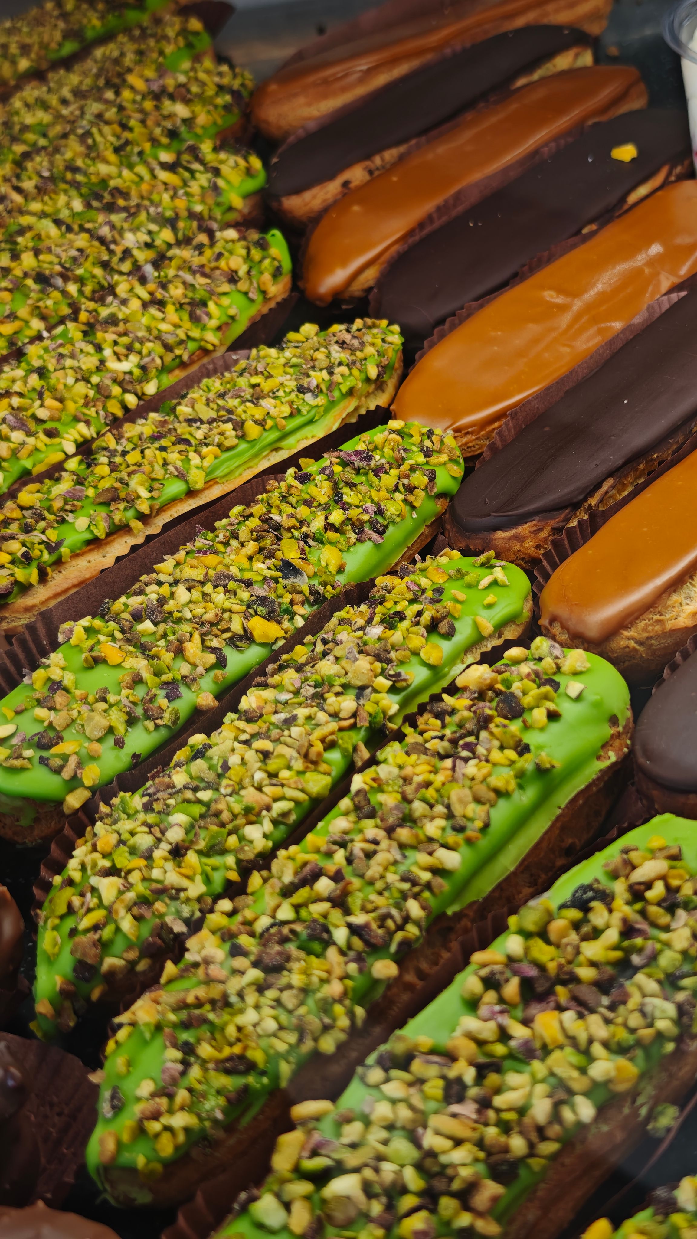 Close-up of assorted eclairs topped with pistachios, chocolate, and caramel.