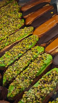 Close-up of assorted eclairs topped with pistachios, chocolate, and caramel.
