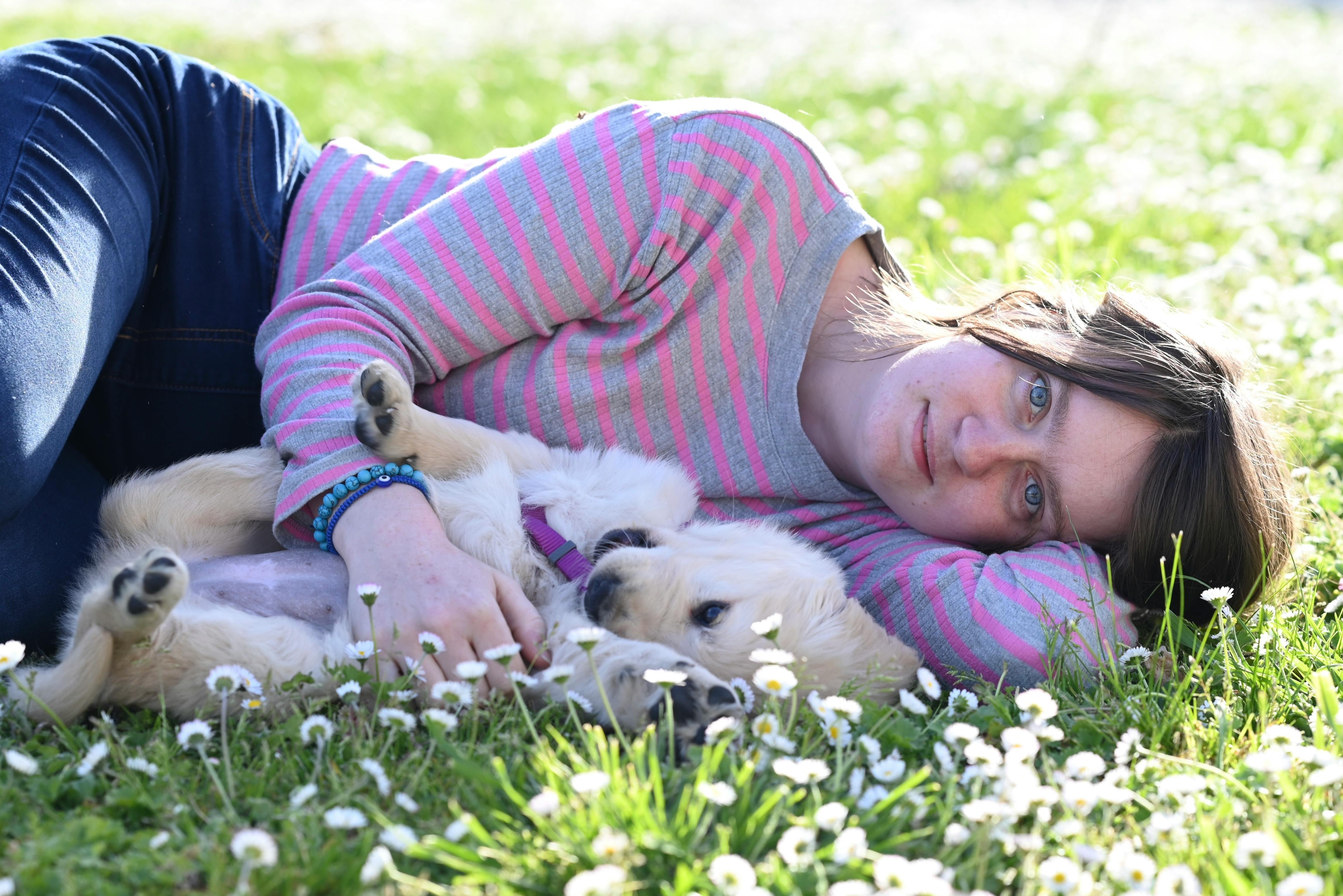 Woman lying in the grass with her golden retriever puppy enjoying a sunny day.