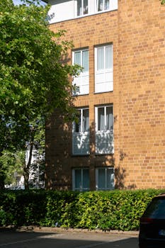 Sunlit brick apartment building facade with leaf shadows and greenery.