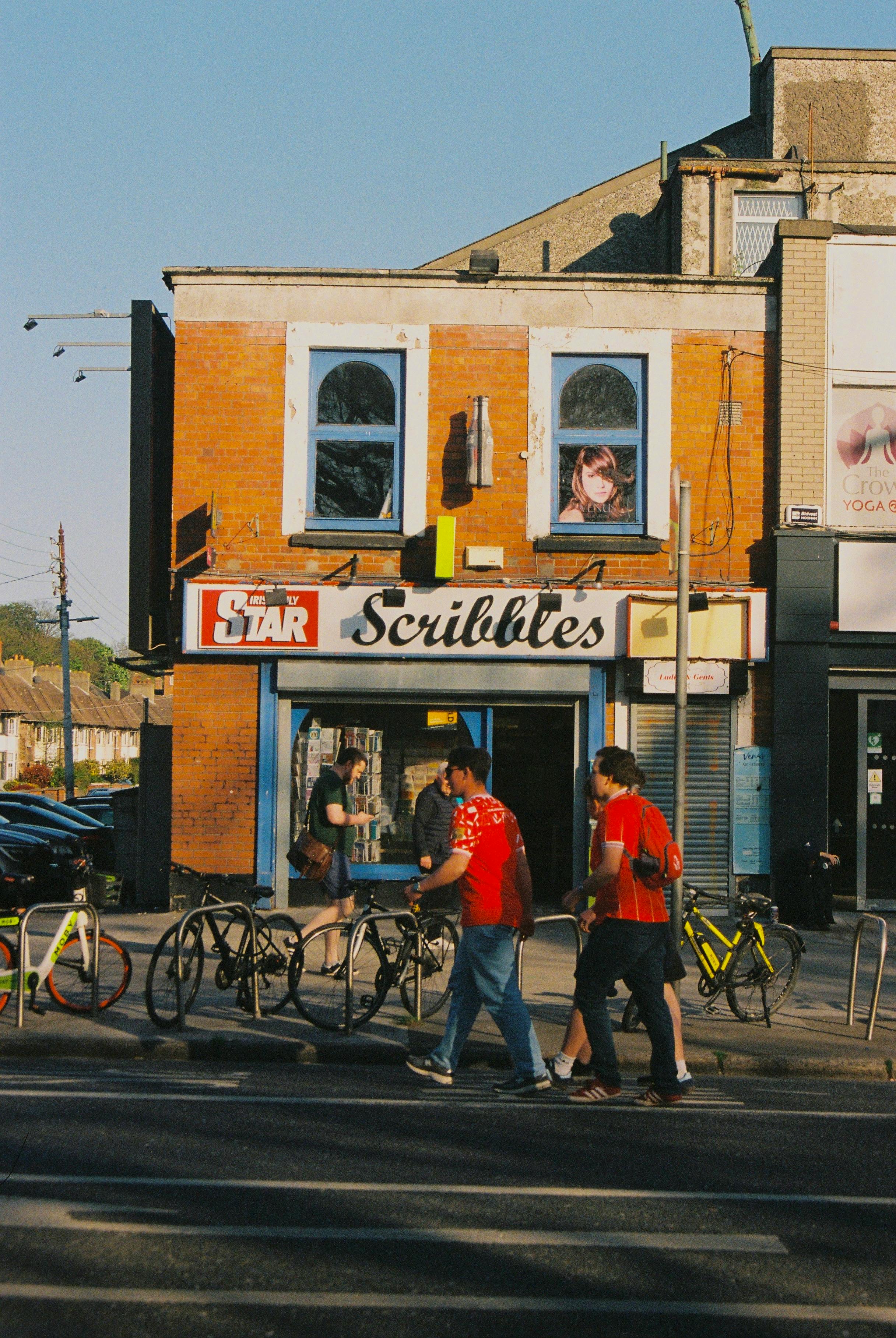 A lively urban street scene featuring bicycles, pedestrians, and shops under the warm daylight.