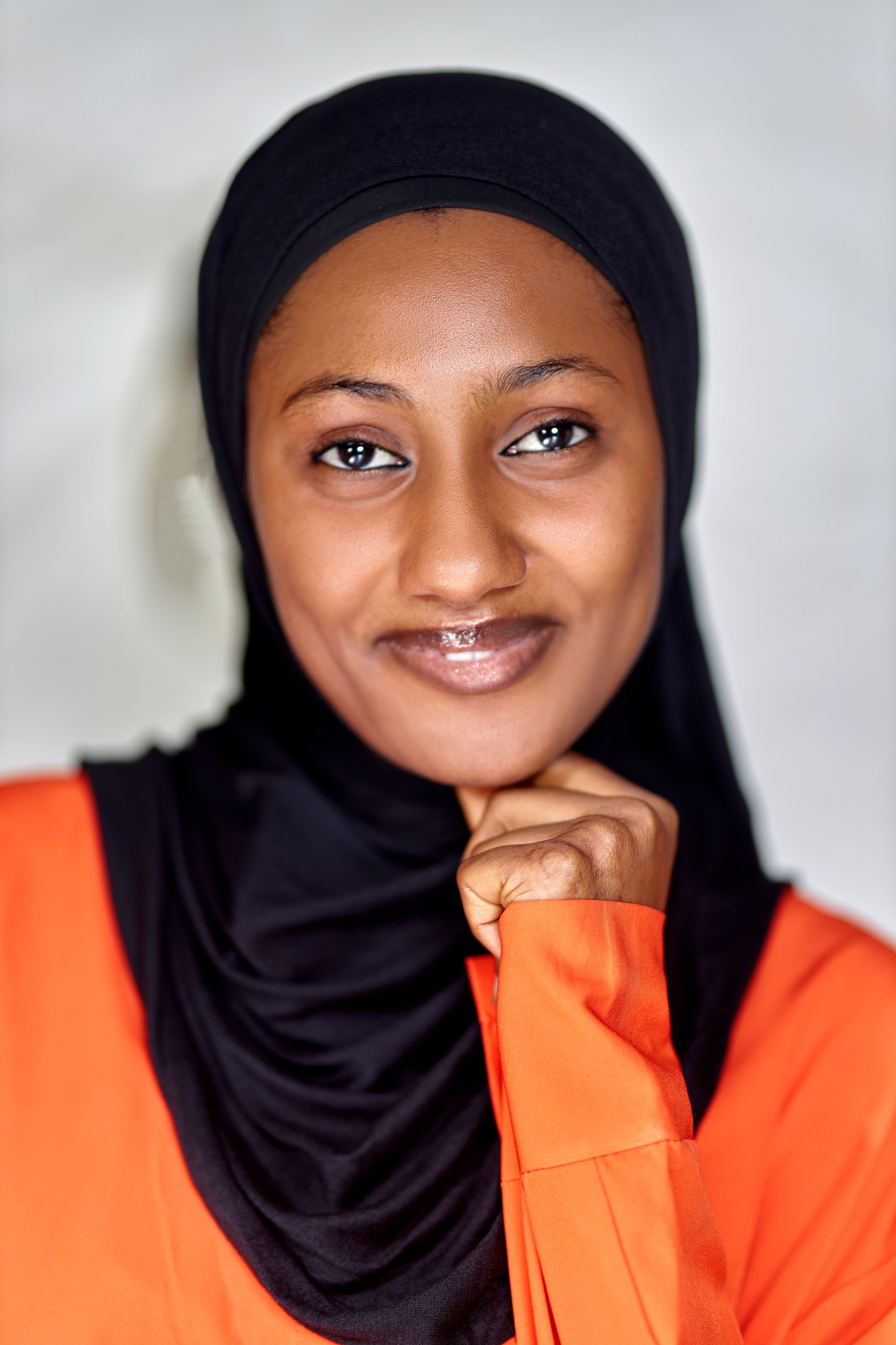 A woman in a hijab smiling warmly with a thoughtful pose indoors.