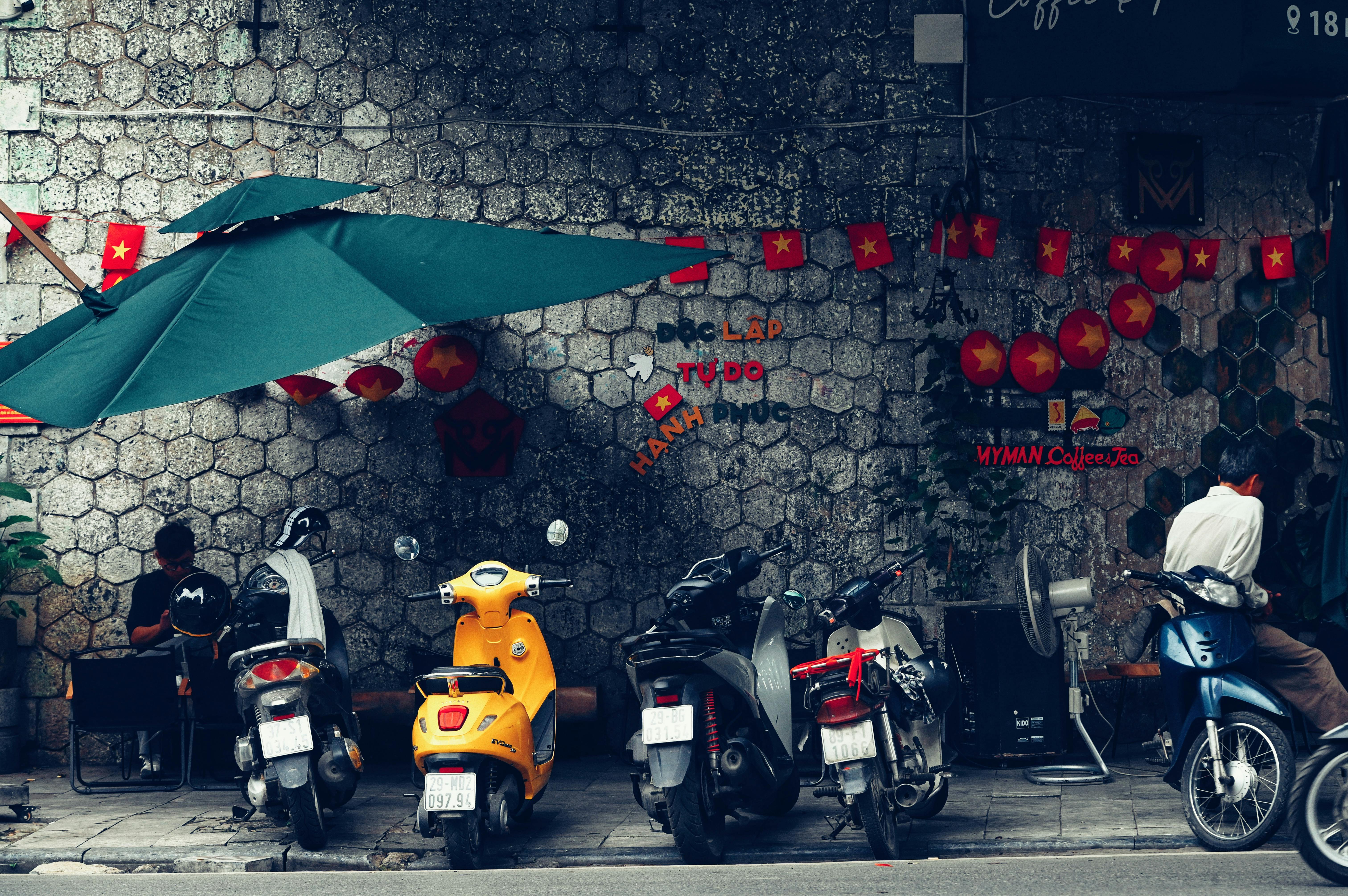Vue de rue urbaine avec des scooters vibrants, une décoration de café et des drapeaux du Vietnam sur un mur texturé.