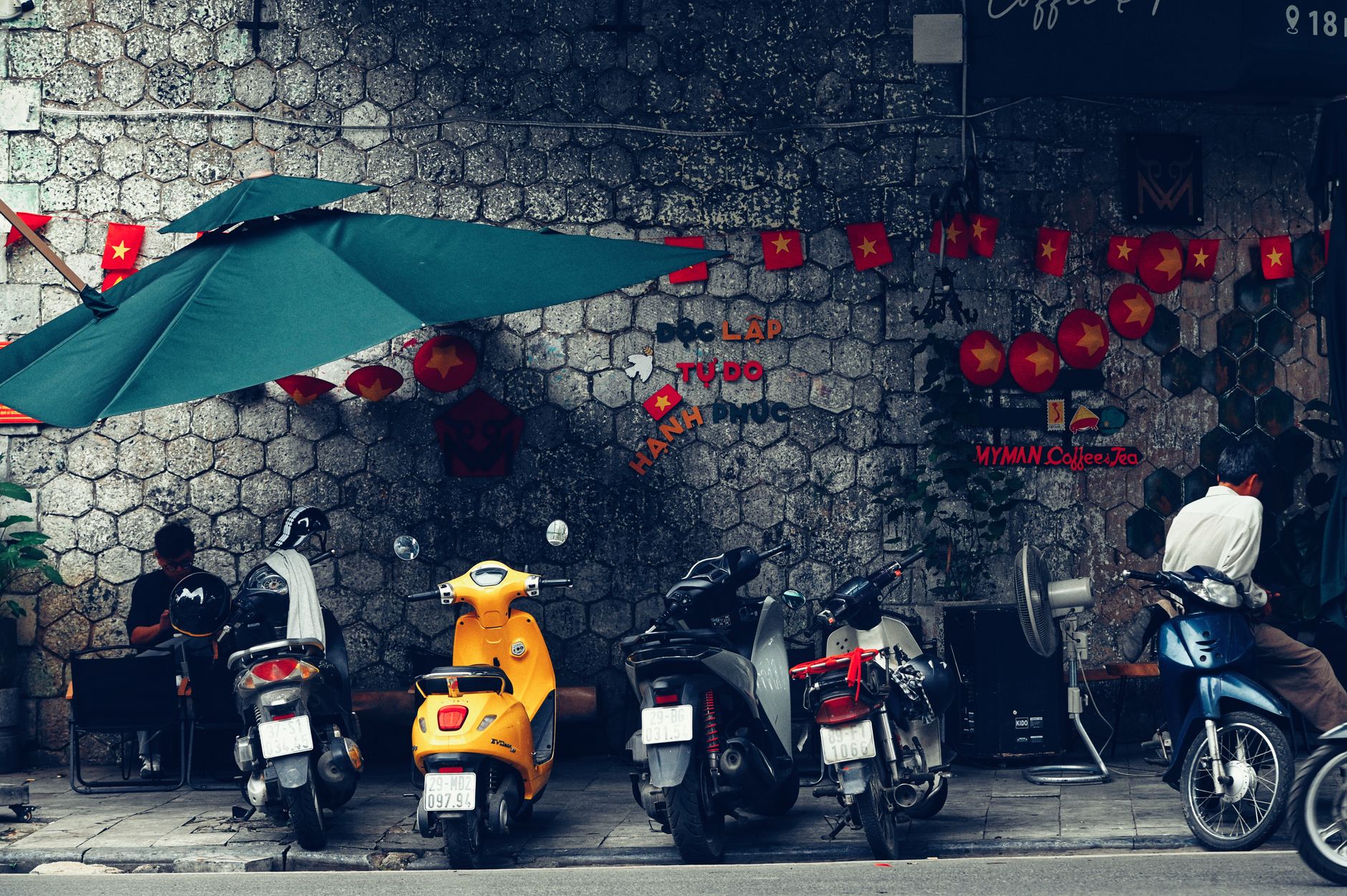 Urban street view featuring vibrant scooters, cafe decor, and Vietnam flags on a textured wall.