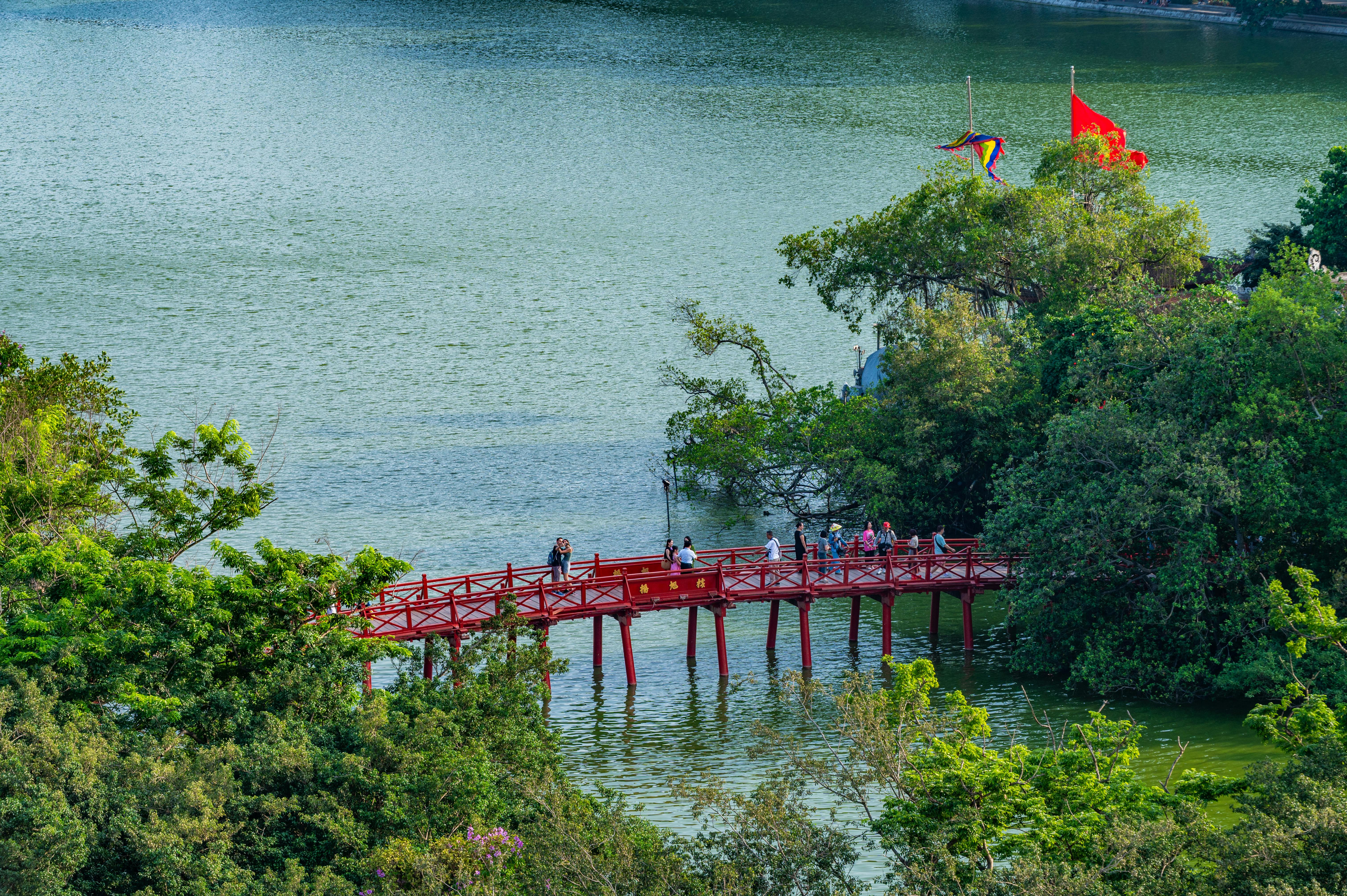 Scenic view of the wooden bridge over Hoan Kiem Lake in Hanoi, Vietnam with lush greenery.