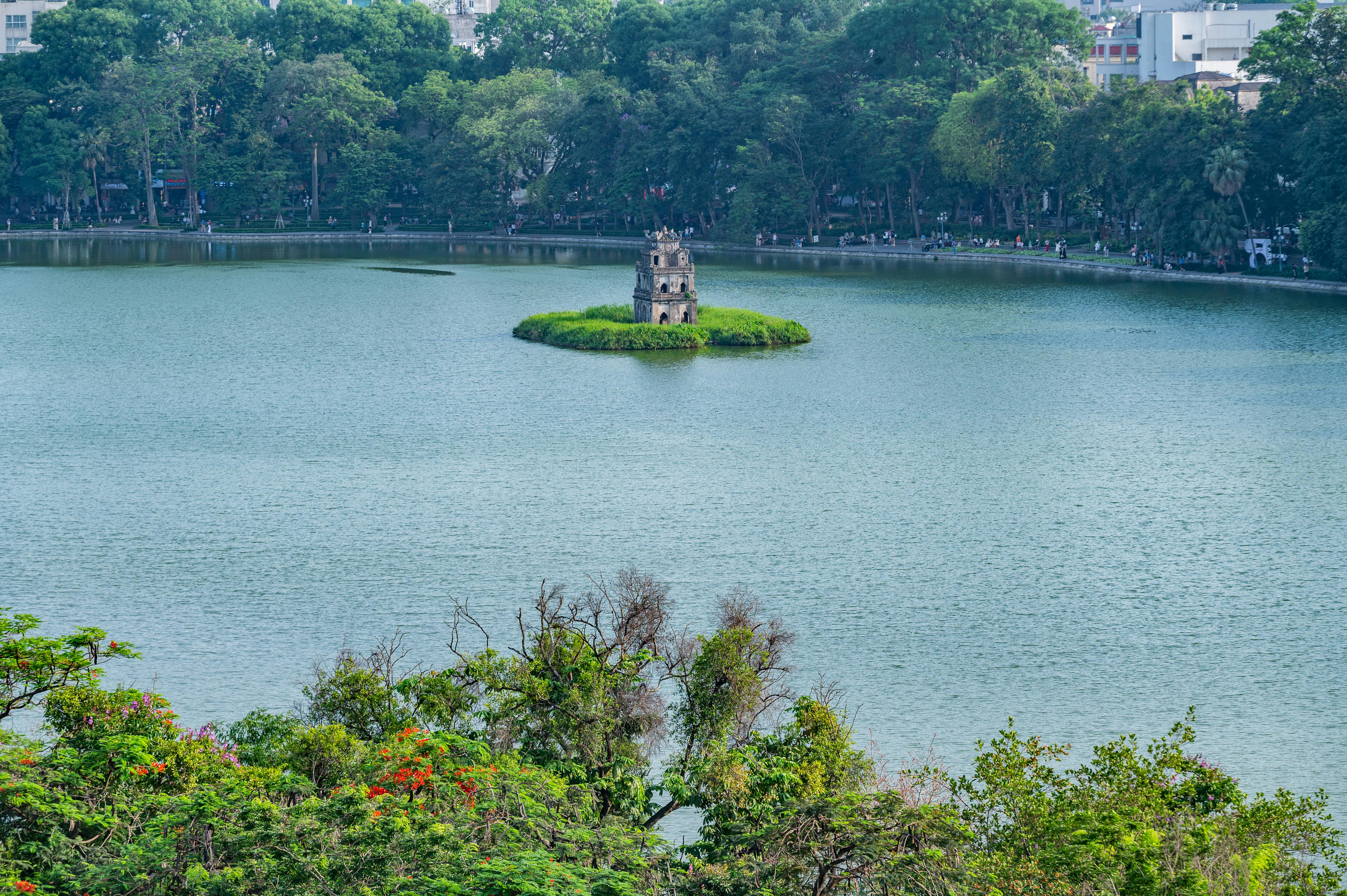 A scenic view of Turtle Tower on Hoan Kiem Lake surrounded by lush greenery in Hanoi, Vietnam.