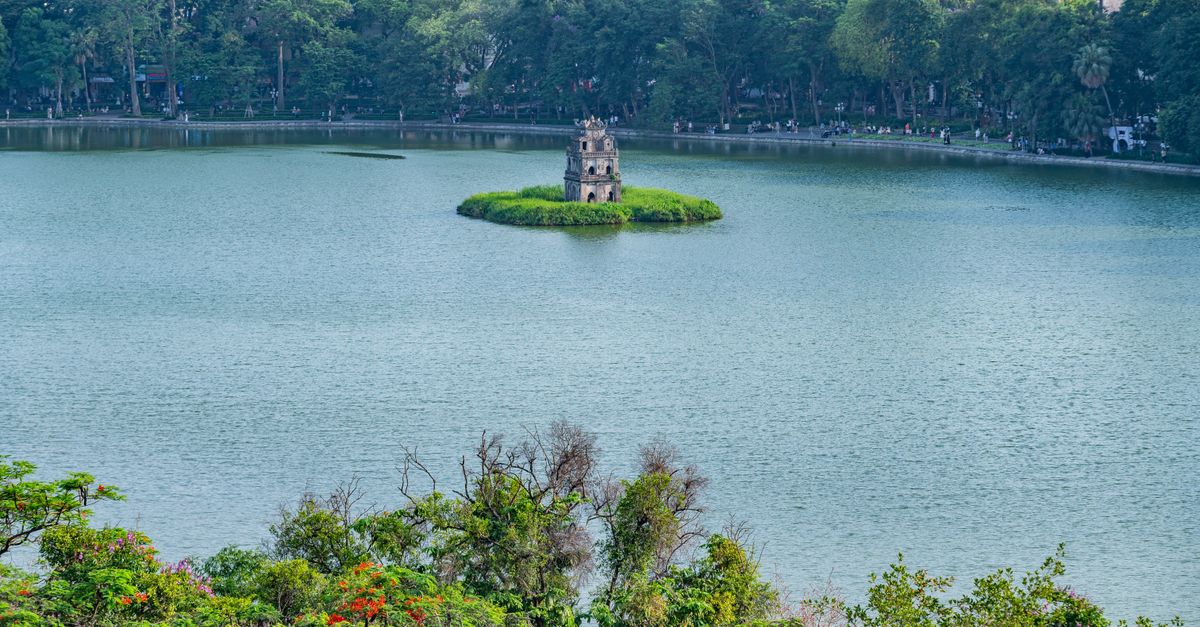 A scenic view of Turtle Tower on Hoan Kiem Lake surrounded by lush greenery in Hanoi, Vietnam.
