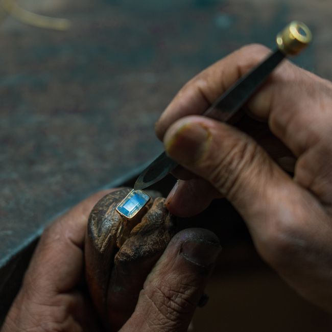 Close-up of artisan setting a blue gemstone into a gold ring with precise craftsmanship.