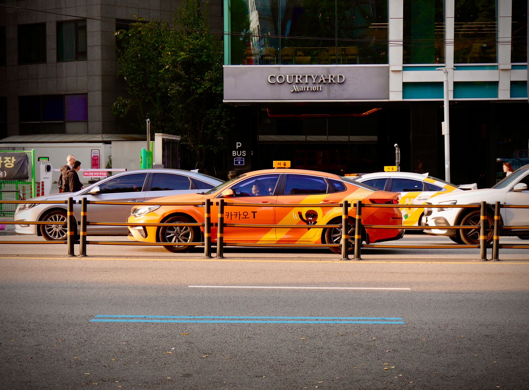 A vivid orange taxi waits on a busy street in front of a Courtyard Marriott hotel.