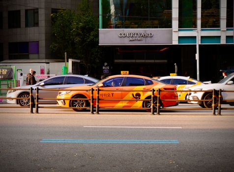 A vivid orange taxi waits on a busy street in front of a Courtyard Marriott hotel.