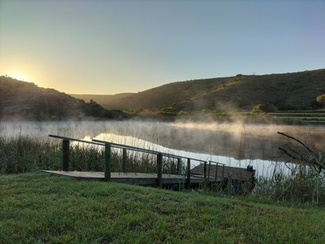 Peaceful sunrise scene featuring mist on river and rustic dock, perfect for serene landscapes.