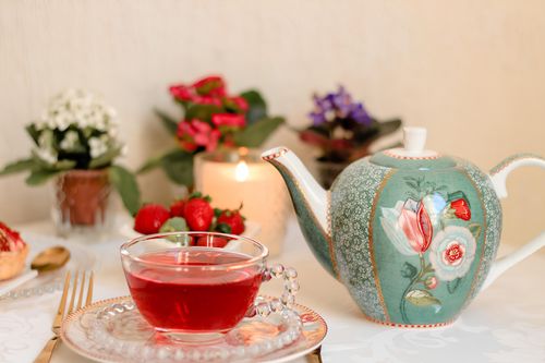 Free Charming tea setup featuring floral teapot, berries, and candlelight for an intimate gathering. Stock Photo