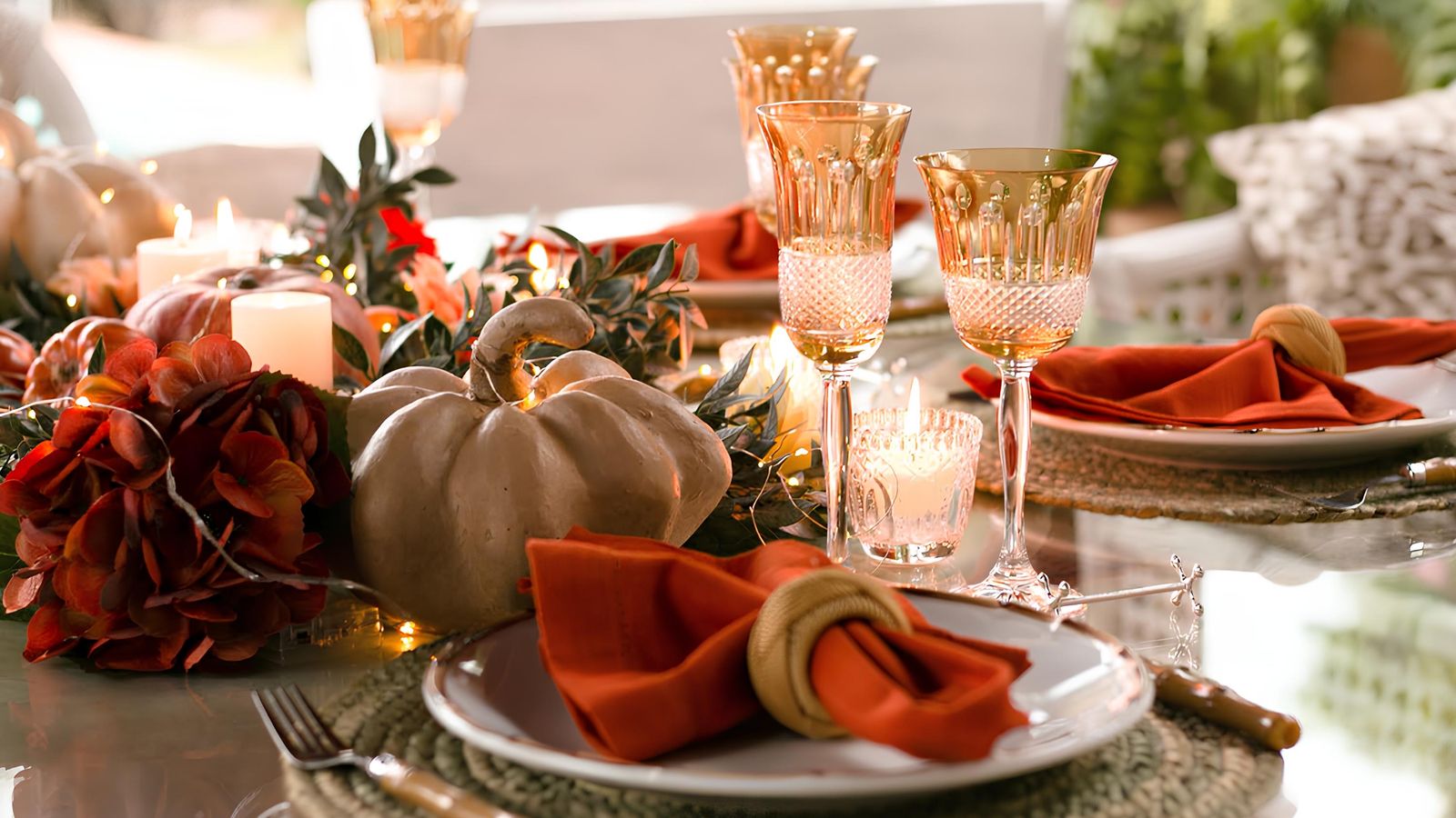 Autumn dining table set with small pumpkins, candles and gold-rimmed wine glasses