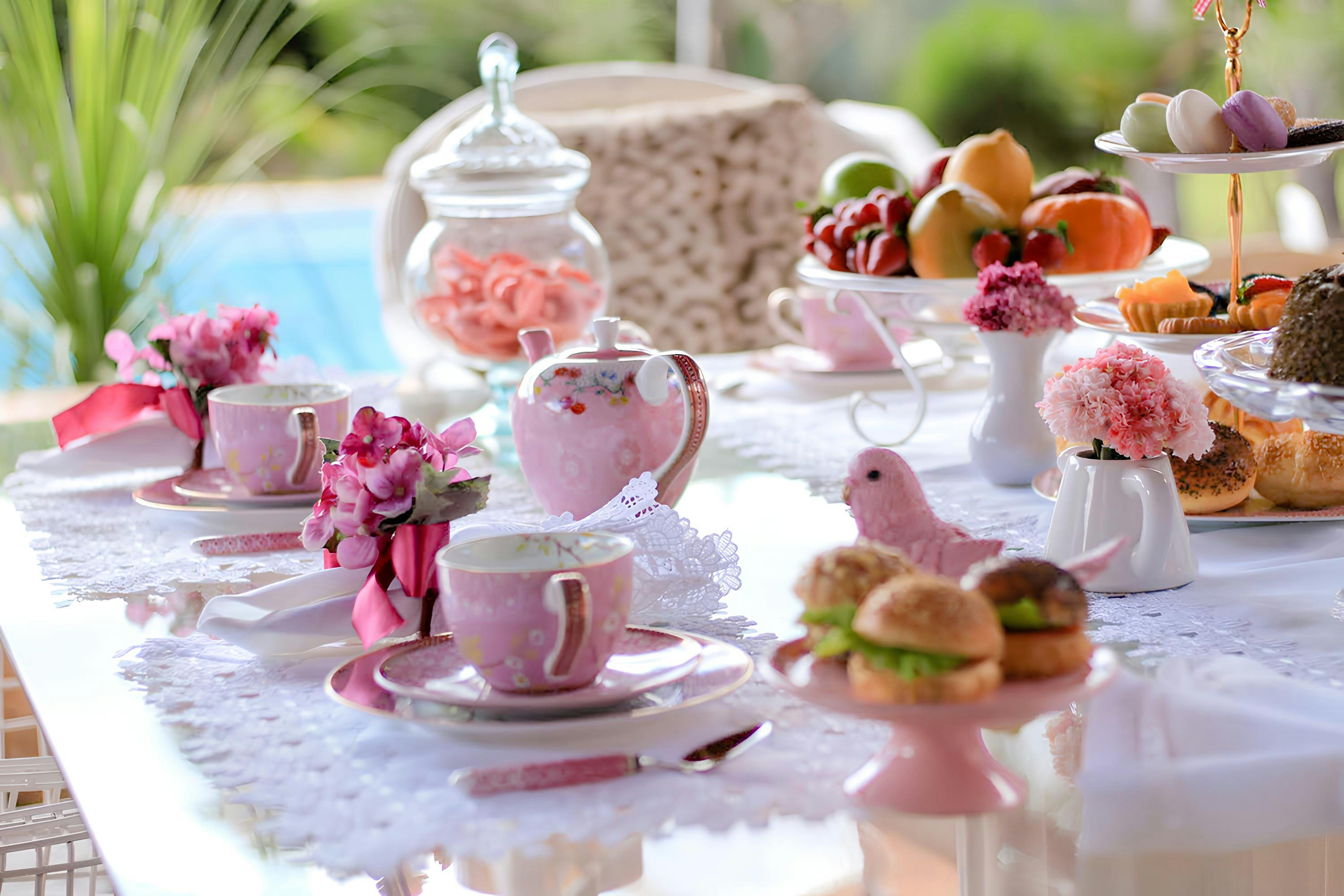 A beautifully arranged outdoor tea party table with pink floral decor and an assortment of treats.