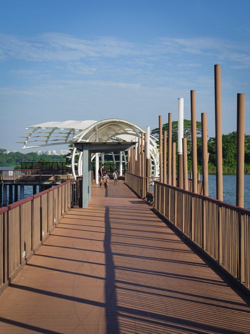 Free Serene view of a wooden boardwalk with a modern pavilion over a peaceful lake. Stock Photo