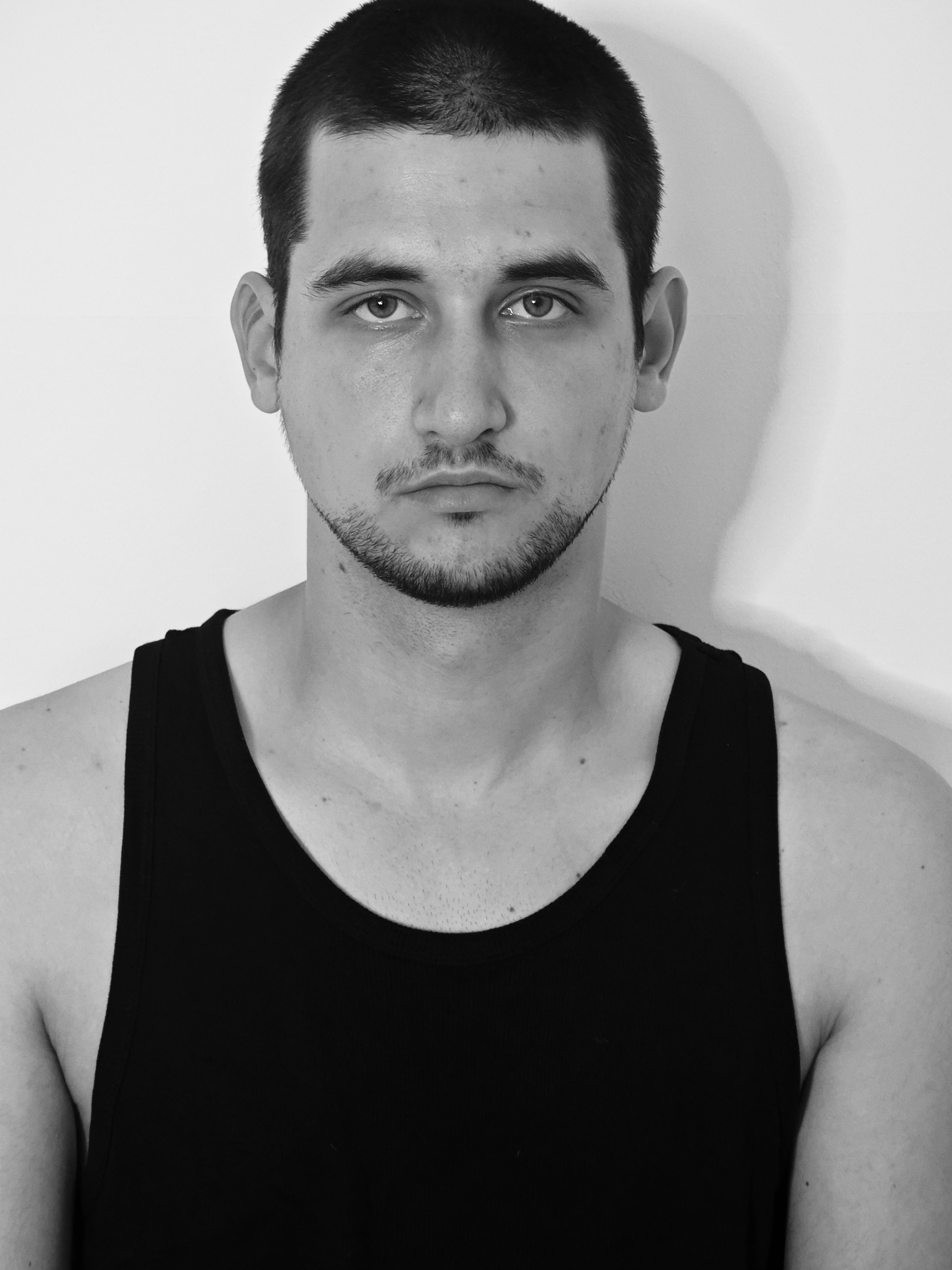 Black and white portrait of a young man wearing a tank top, looking directly at the camera.