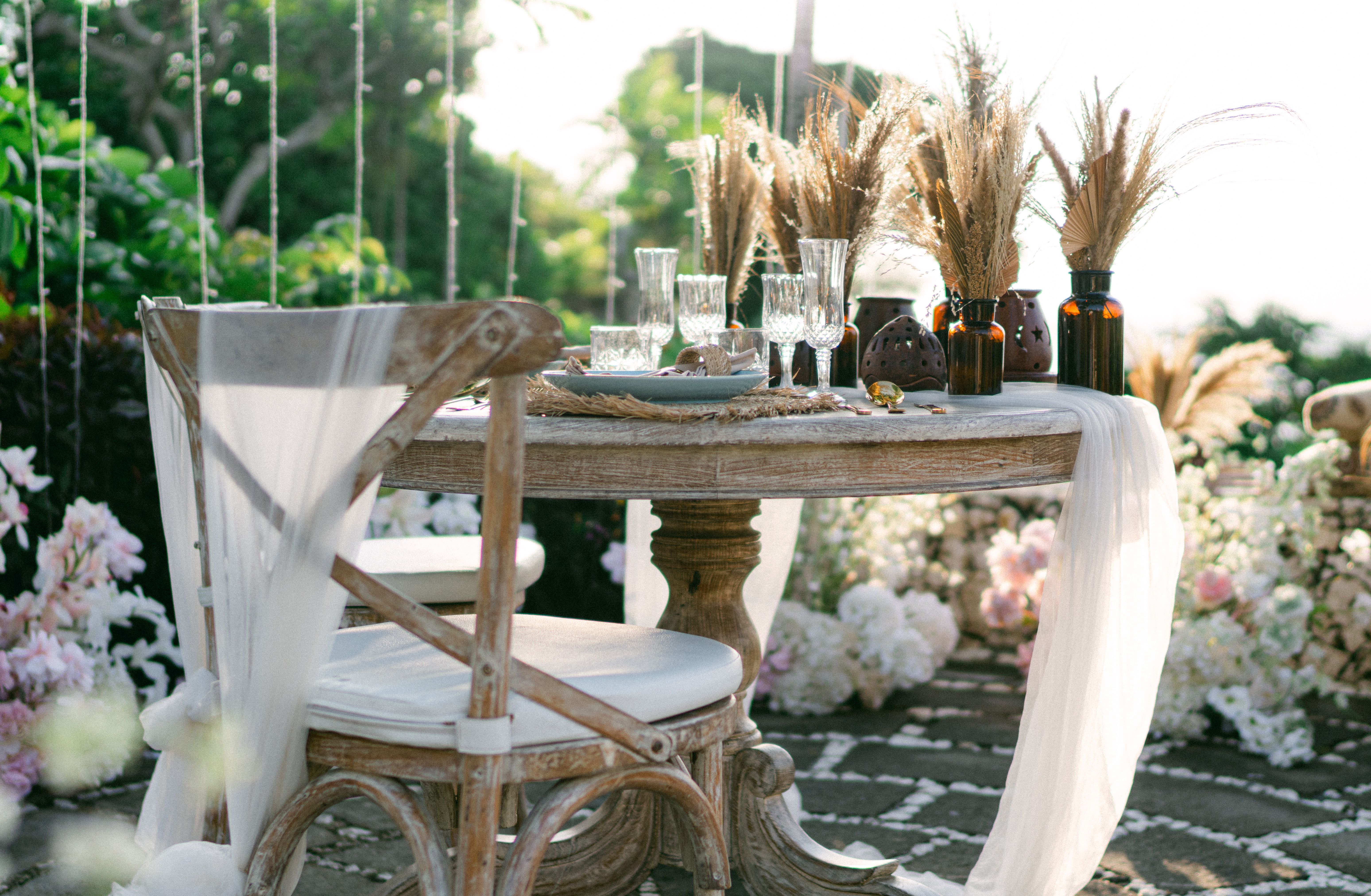 Elegant outdoor table setting with rustic decor, pampas grass, and flowers, perfect for a wedding or special event.