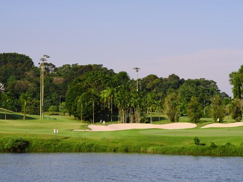 Free Peaceful golf course with lush greenery and sand traps by a river under a clear blue sky. Stock Photo