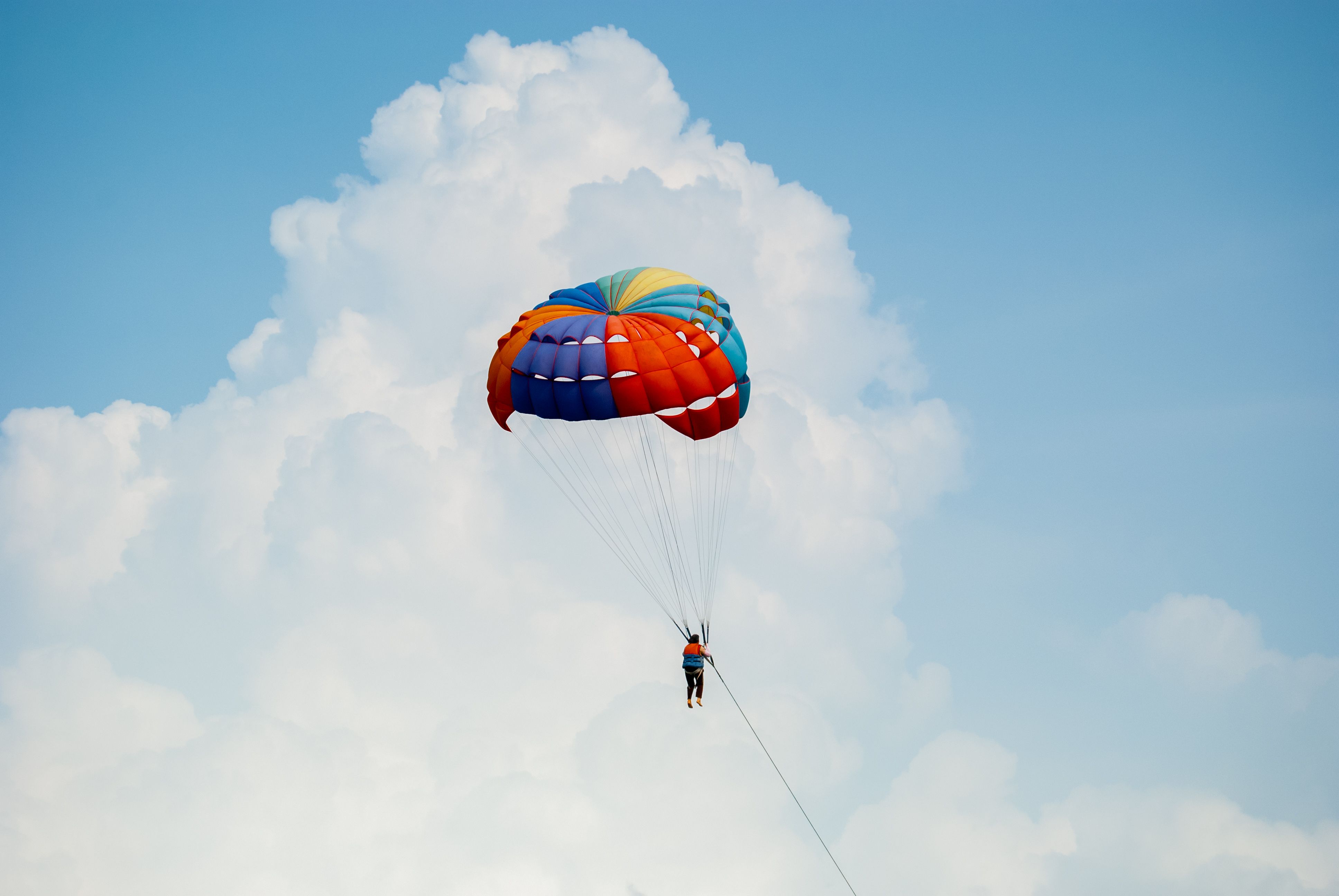 Gratis Un paracadute vivace con una persona che si libra sullo sfondo di soffici nuvole e un cielo azzurro e terso. Foto a disposizione