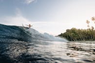 在印度尼西亚的一个阳光明媚的日子里，冲浪者骑在大浪附近的热带海滩上