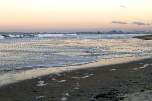 Free Experience a serene sunset at Guaratuba Beach, Brazil, with gentle waves and scenic views of distant mountains. Stock Photo