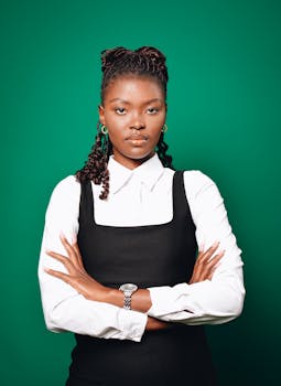 Photo by Olerato Motshebe Portrait of a confident businesswoman with arms crossed, wearing formal attire against a green backdrop.