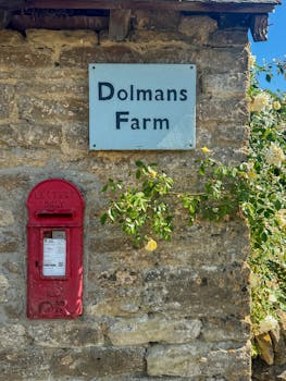 Charming rural scene of Dolmans Farm with a bright red postbox and blooming yellow roses, set against a stone wall.