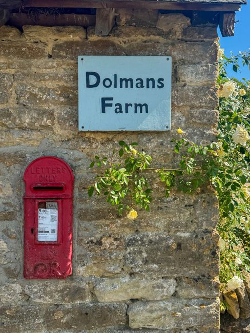 Charming rural scene of Dolmans Farm with a bright red postbox and blooming yellow roses, set against a stone wall.
