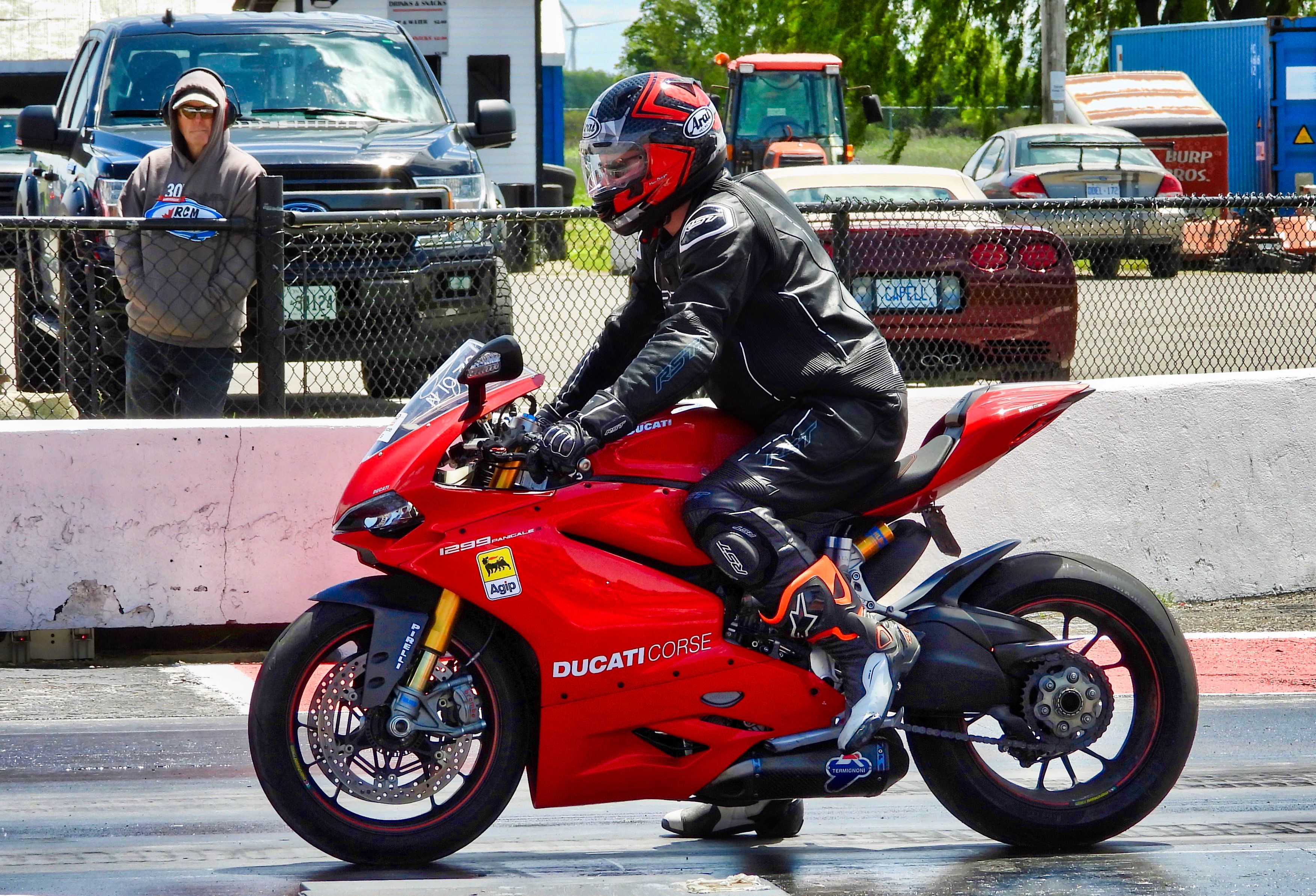 A motorcyclist in full gear races a red Ducati on a sunny day in Cayuga, Ontario.
