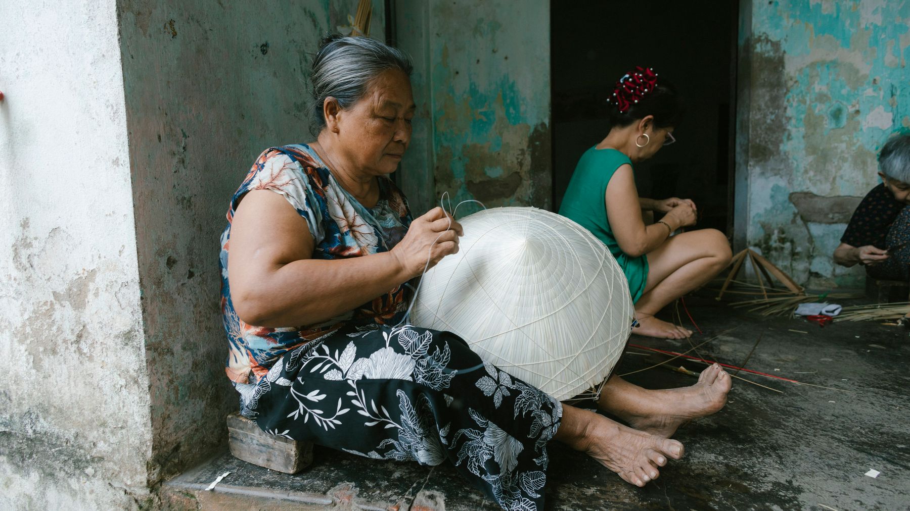 Elderly women skillfully crafting traditional conical hats in a rustic outdoor setting.