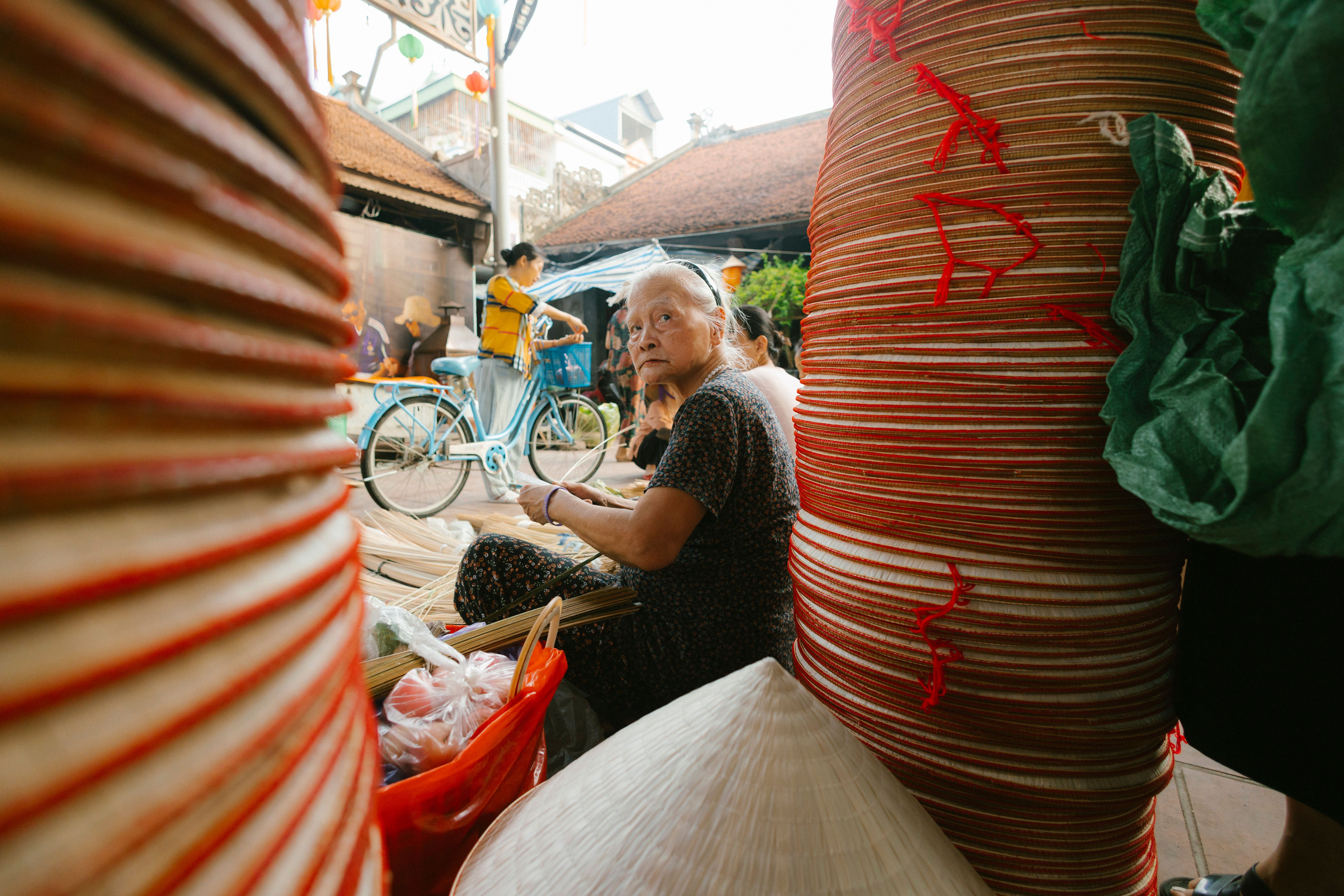 elderly Vietnamese woman in a traditional ao dai taking a portrait with a vintage camera at a crowded market stall
