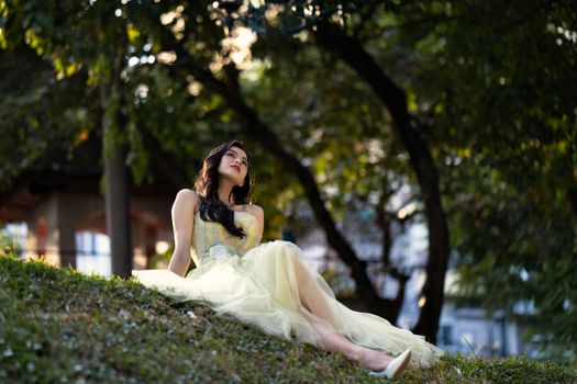 A serene moment captured of a woman in an elegant dress relaxing on a sunny hill in a park.
