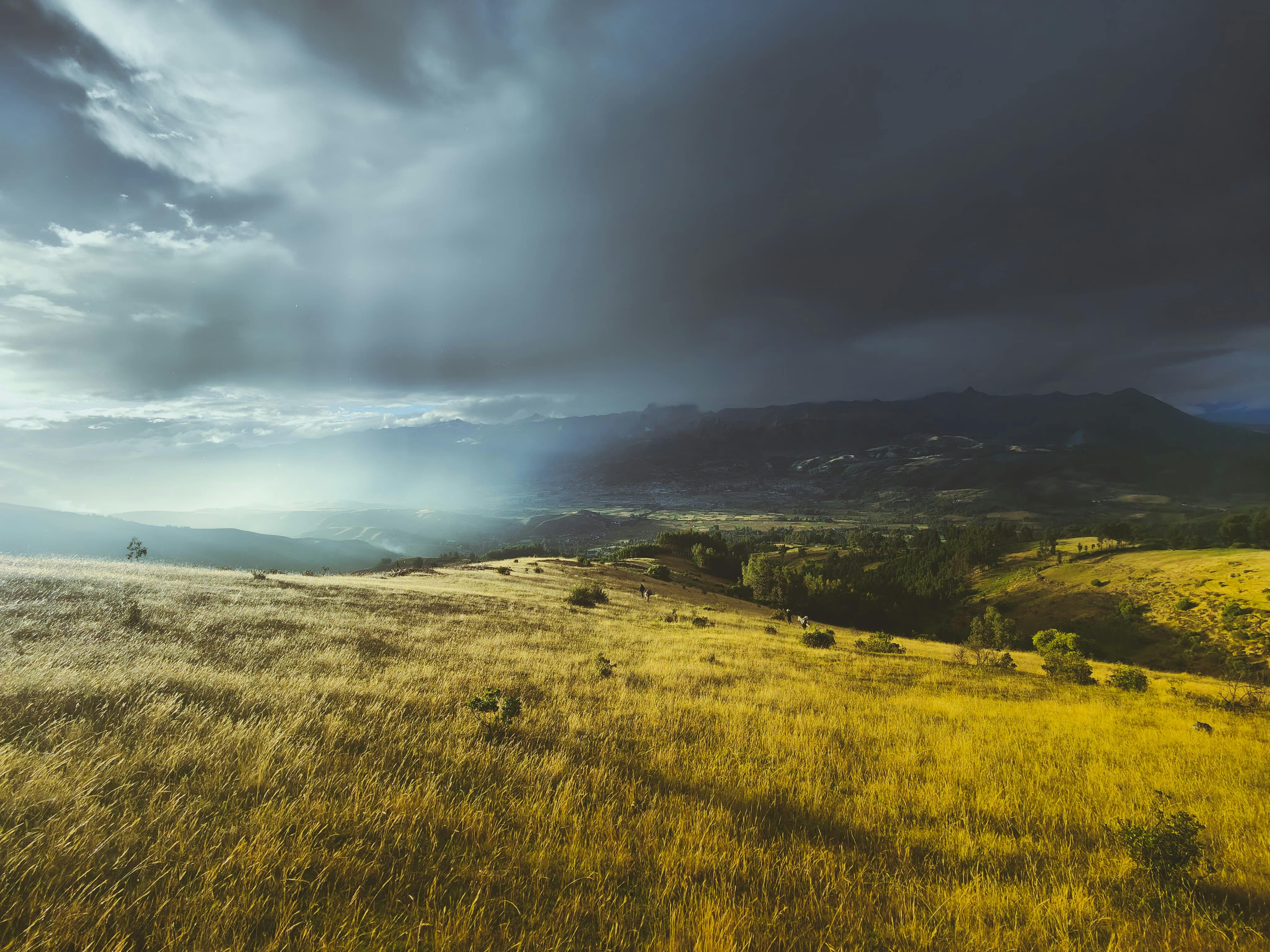 Dramatic sunset over golden fields in Ancahuasi, Cuzco, Peru, with dark storm clouds.
