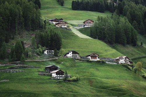Free Scenic view of rustic alpine houses nestled in lush green hills surrounded by dense forest. Stock Photo