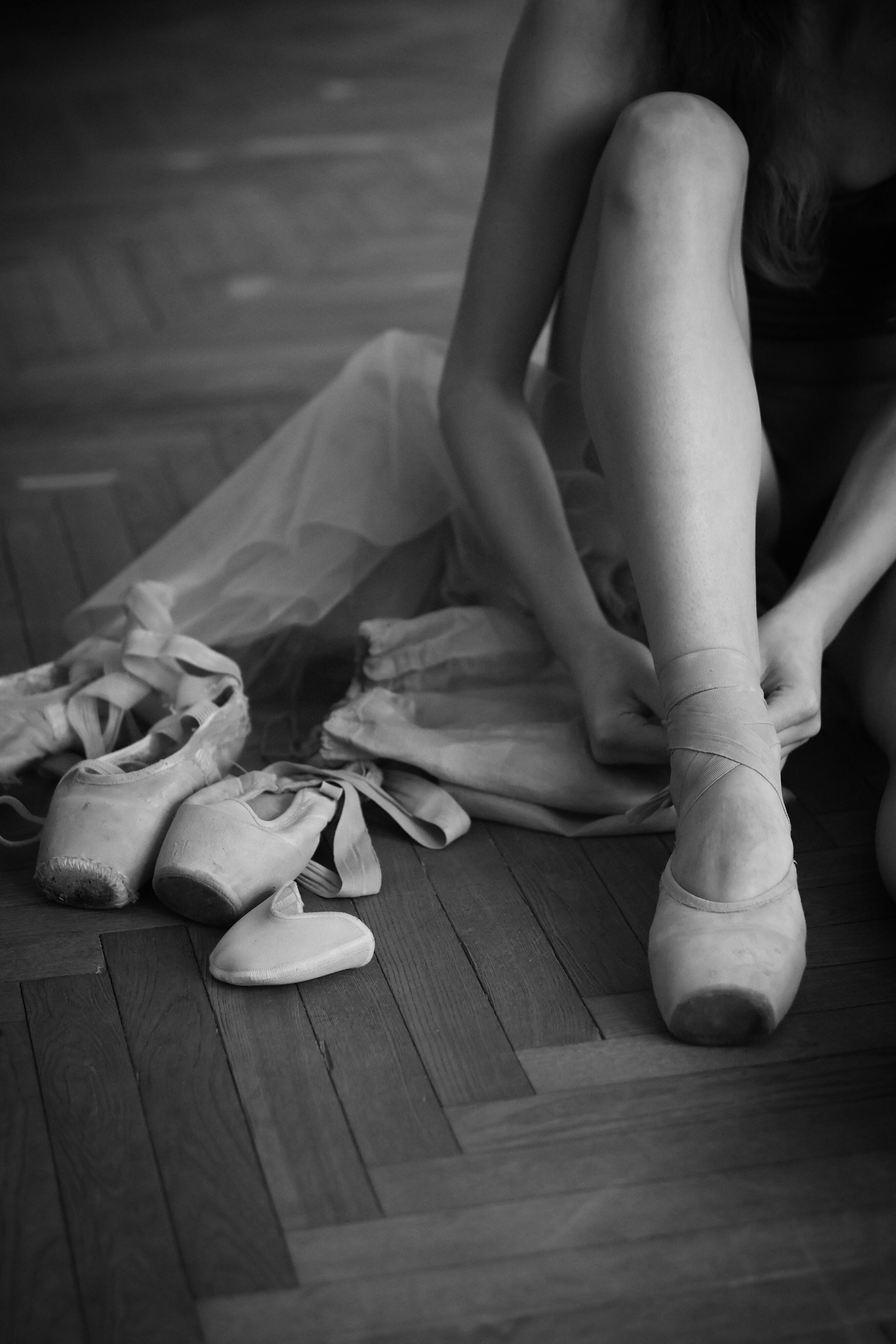 Elegant ballet dancer tying pointe shoes, preparing for rehearsal.