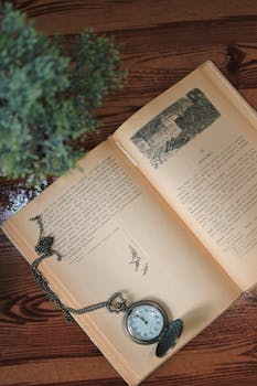 Antique pocket watch rests on an open vintage book atop a polished wooden table.