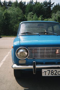 Classic blue vintage car parked outdoors in sunlight near forested area.