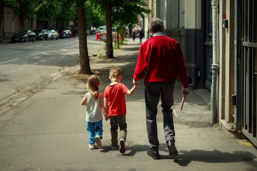 A senior adult and two children walking down a sunny street in Lille, France.