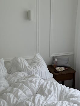 Minimalist bedroom with white bedding and a wooden nightstand, perfect for relaxation.
