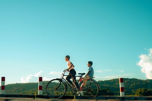 Two boys cycling through the serene countryside of Bangladesh on a sunny day.