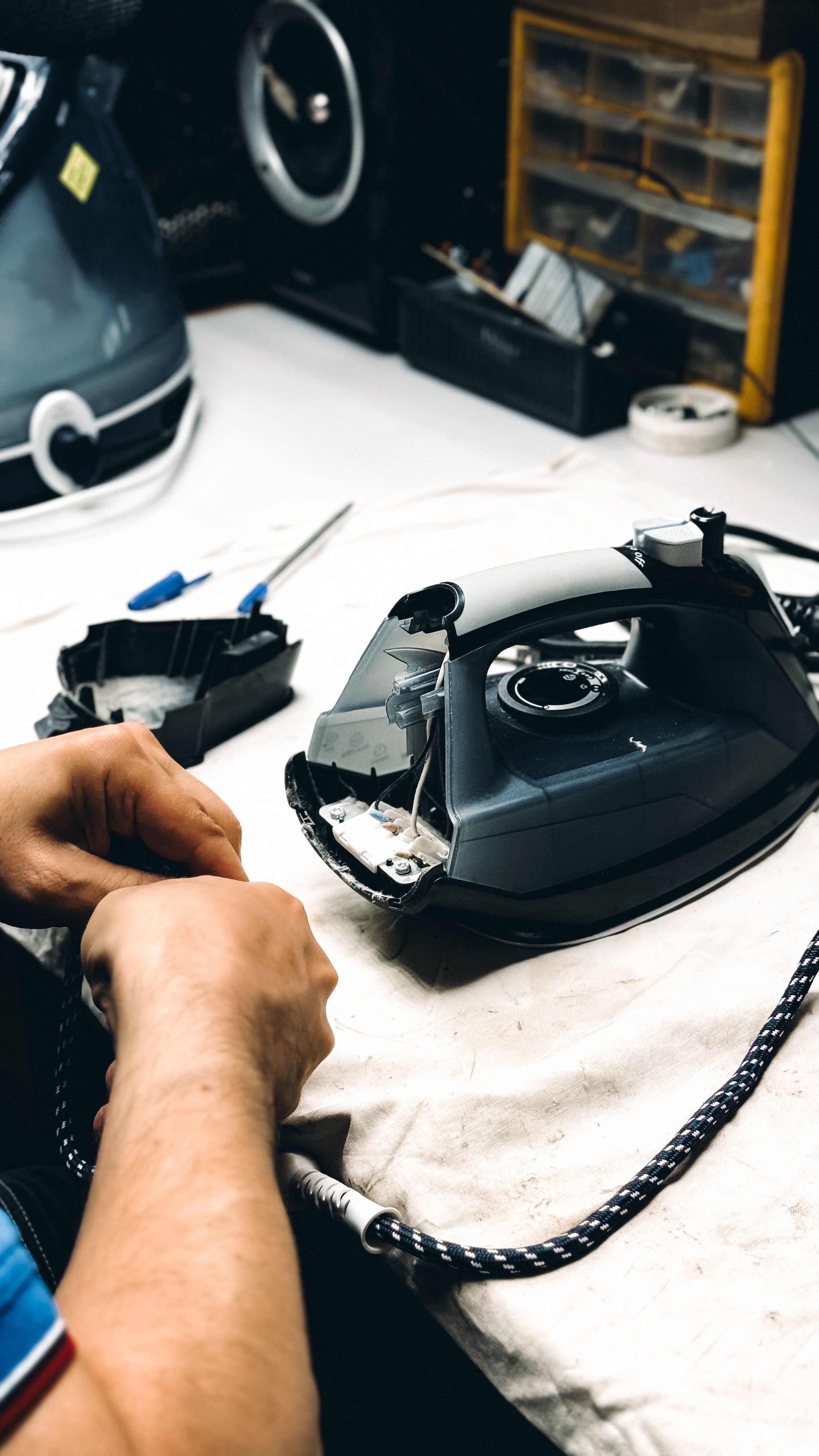Hands working on repairing an iron in a workshop. Tools and parts are visible.