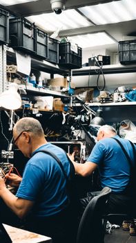 Two adult craftsmen busy working in a cluttered workshop filled with tools.