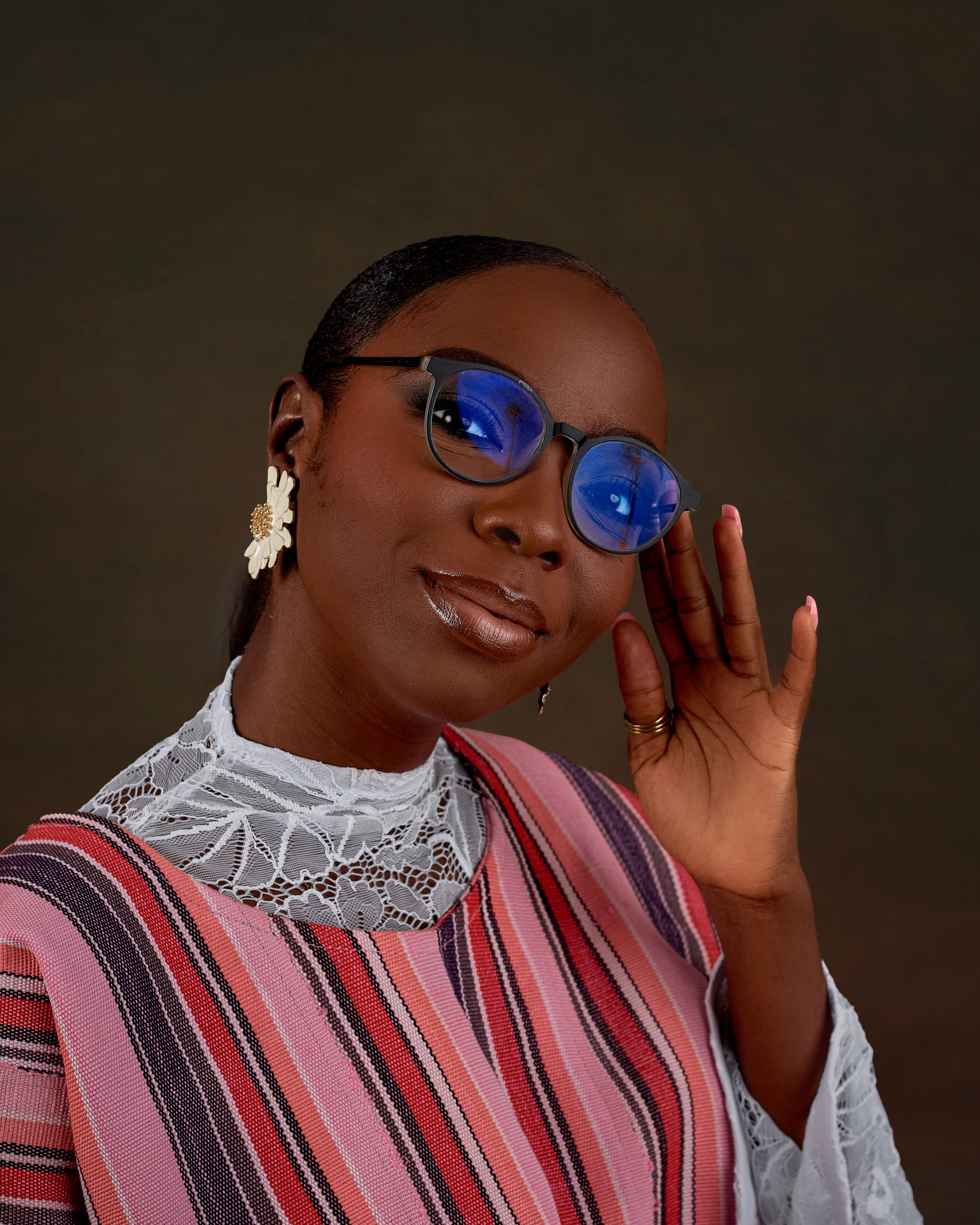 A fashionable woman poses with confidence, wearing vibrant clothing and blue glasses.