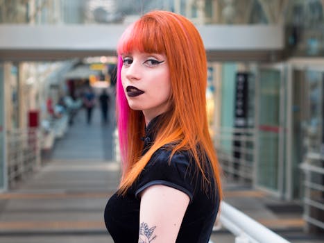 Stylish woman with orange and pink hair in an indoor architectural setting, showcasing bold fashion.