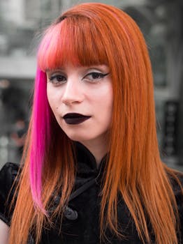 Portrait of a woman with striking orange and pink hair indoors, showcasing bold makeup and unique style.