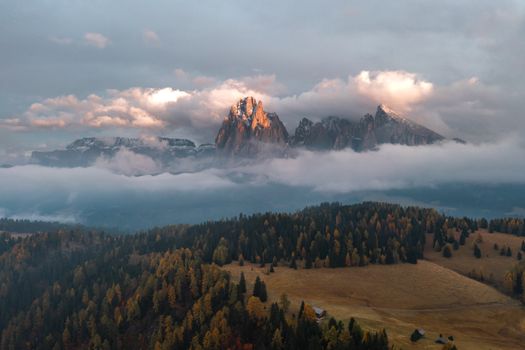 Stunning aerial view of Dolomites peak surrounded by clouds and trees at sunset in Veneto, Italy.