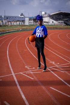 Confident woman holding basketball on outdoor running track in Kaduna, Nigeria.