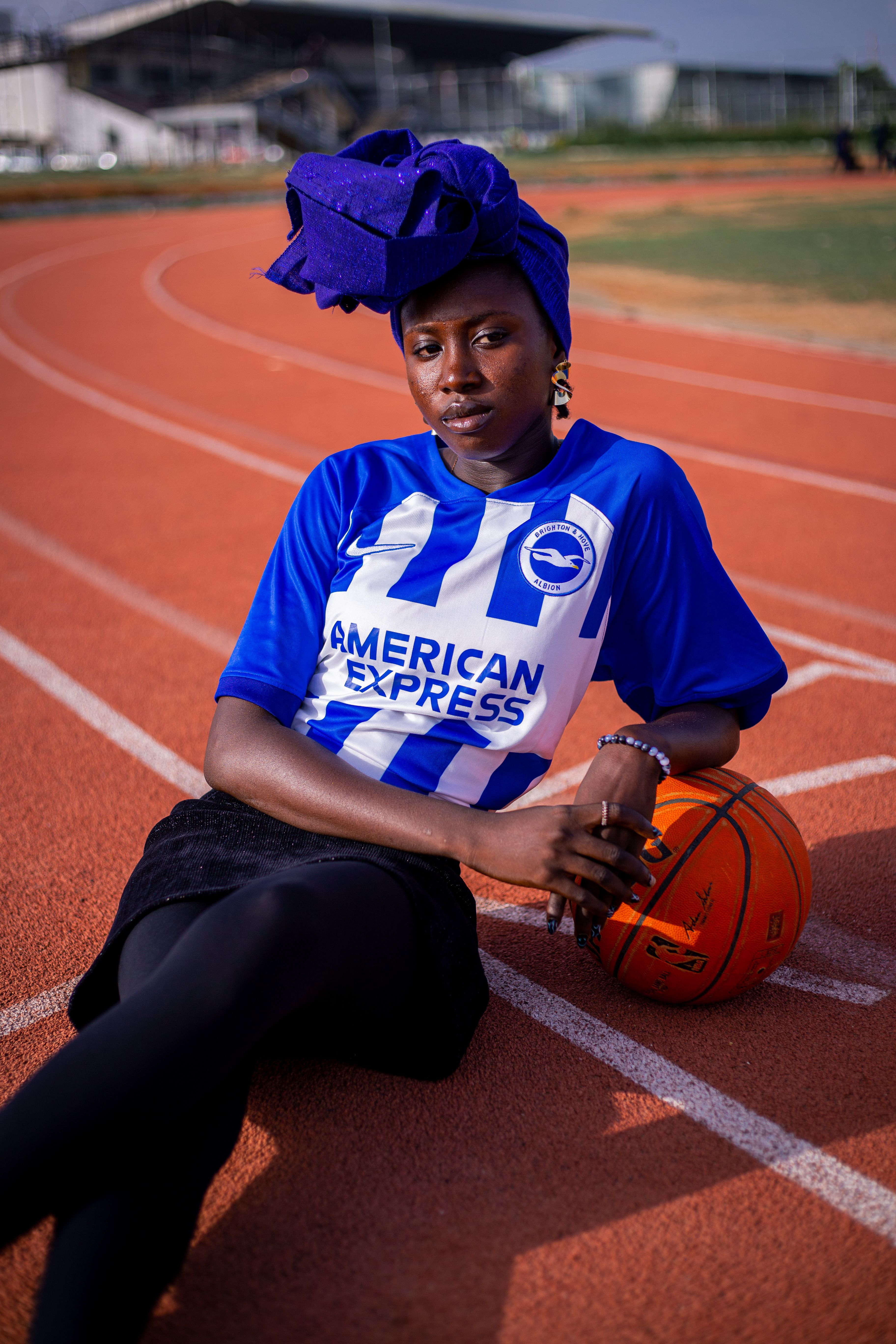 Woman lounging on track in Brighton & Hove Albion jersey holding basketball.